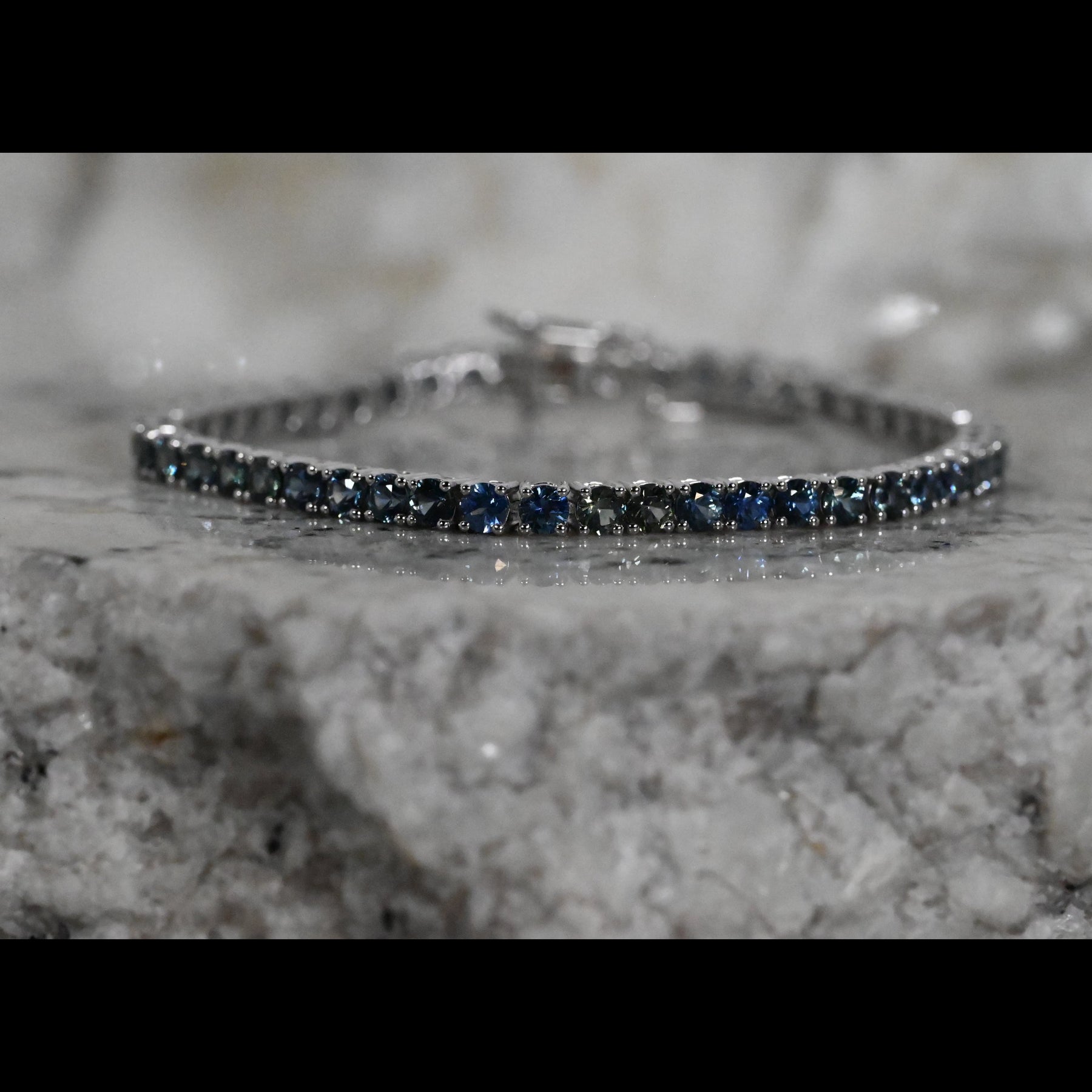 A close-up of a tennis bracelet featuring round dark blue Montana sapphires a white gold setting