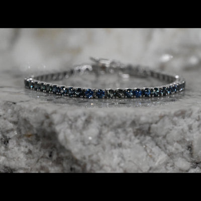 A close-up of a tennis bracelet featuring round dark blue Montana sapphires a white gold setting