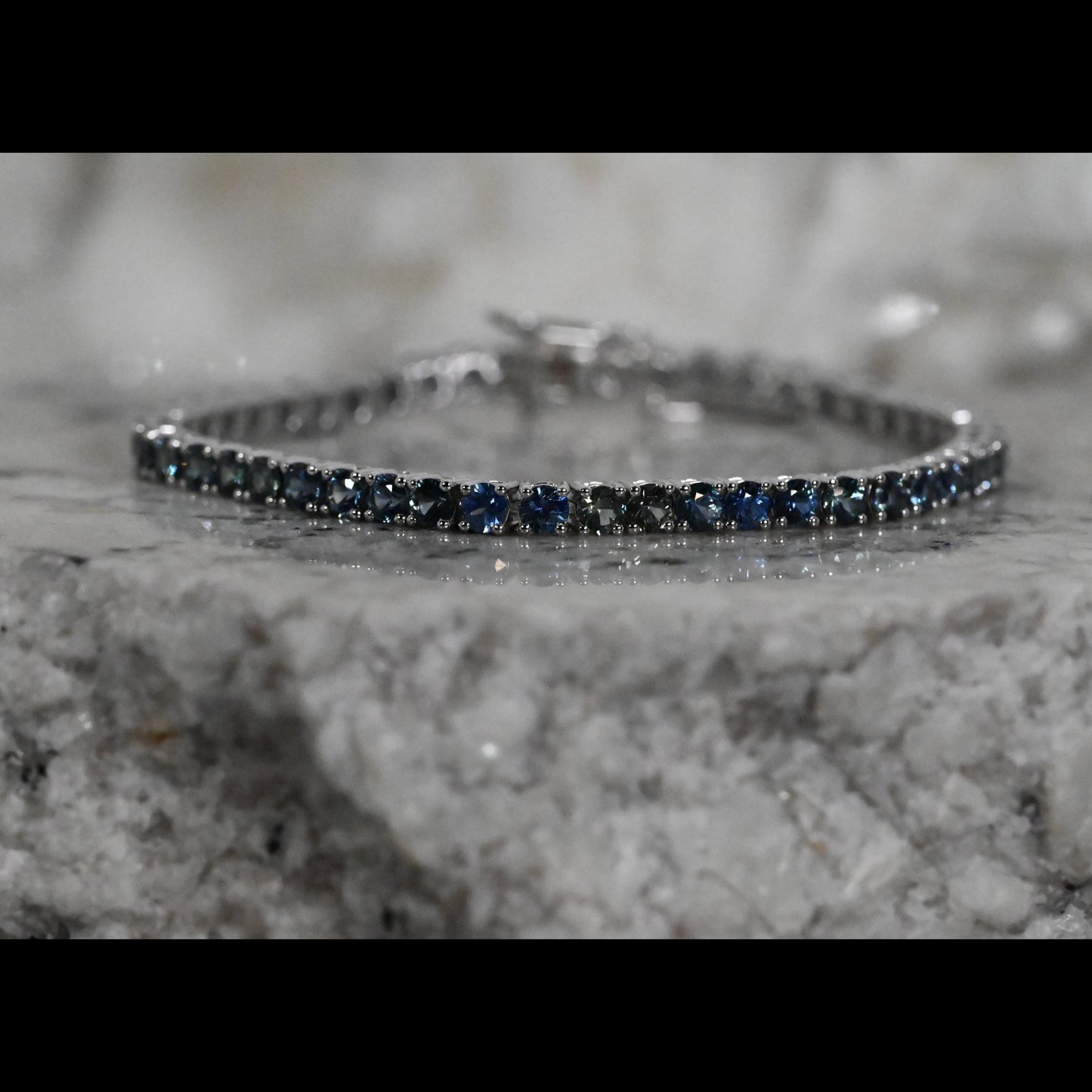 A close-up of a tennis bracelet featuring round dark blue Montana sapphires a white gold setting
