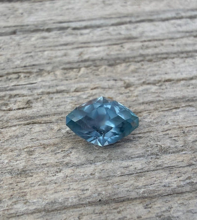 A large faceted marquise-cut blue Montana sapphire,  resting on a textured, weathered wood surface.