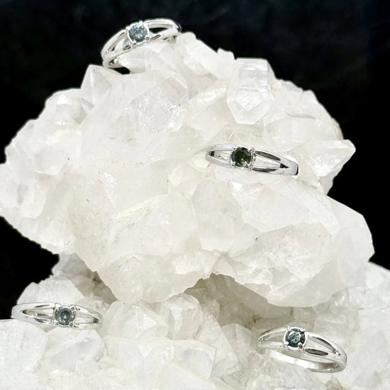 Silver rings with green gemstones on a white crystal rock against a black background