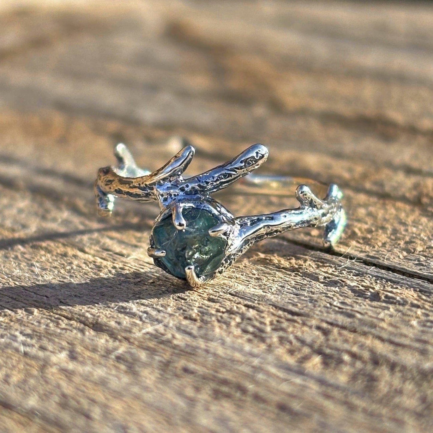 Silver branch-shaped ring on a wooden surface with an uncut Montana sapphire