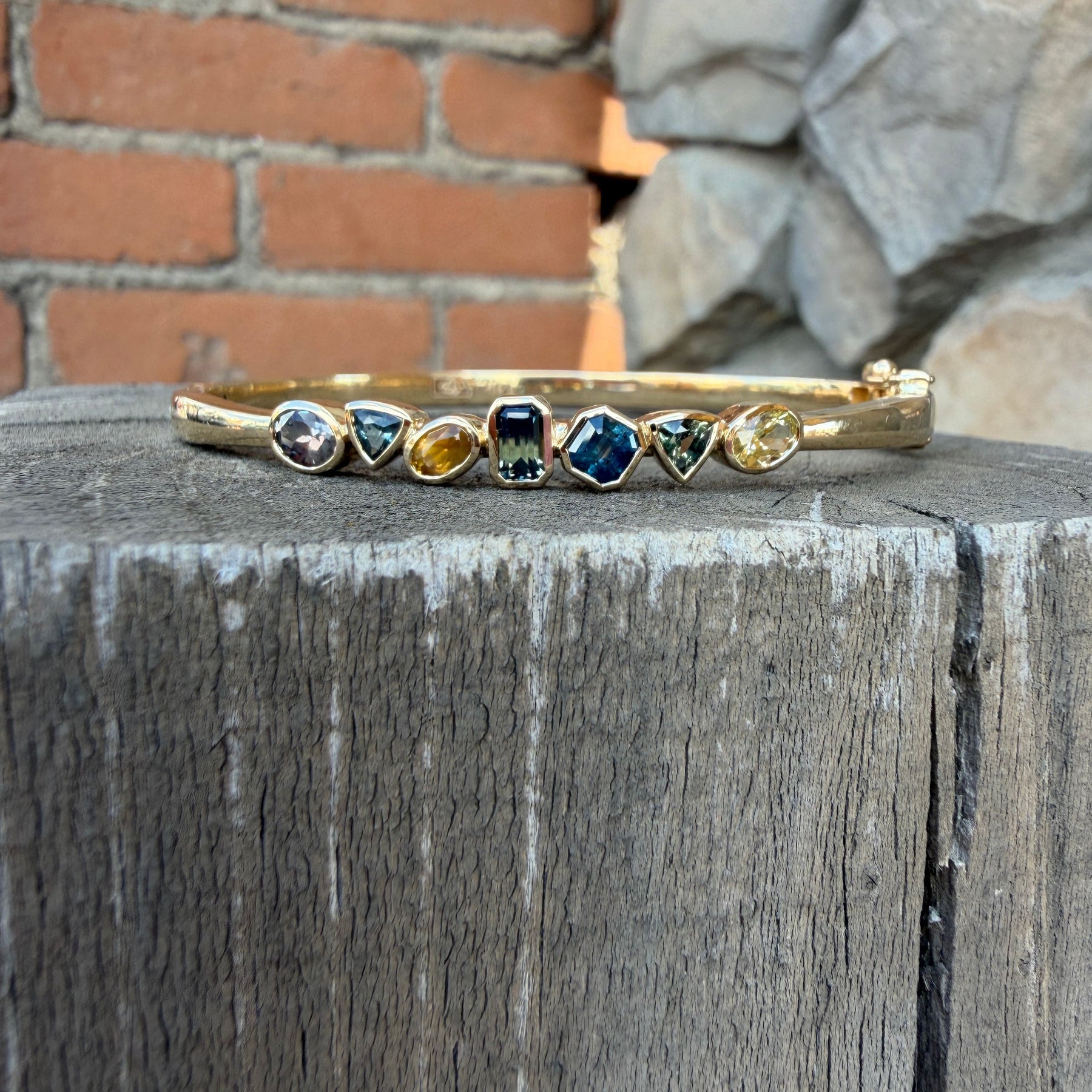 A gold bangle bracelet with seven Montana sapphires in multi colors.  Oval Bangle and bezel set sapphires. 