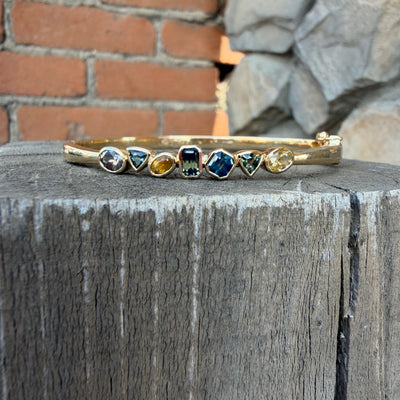 A gold bangle bracelet with seven Montana sapphires in multi colors.  Oval Bangle and bezel set sapphires. 