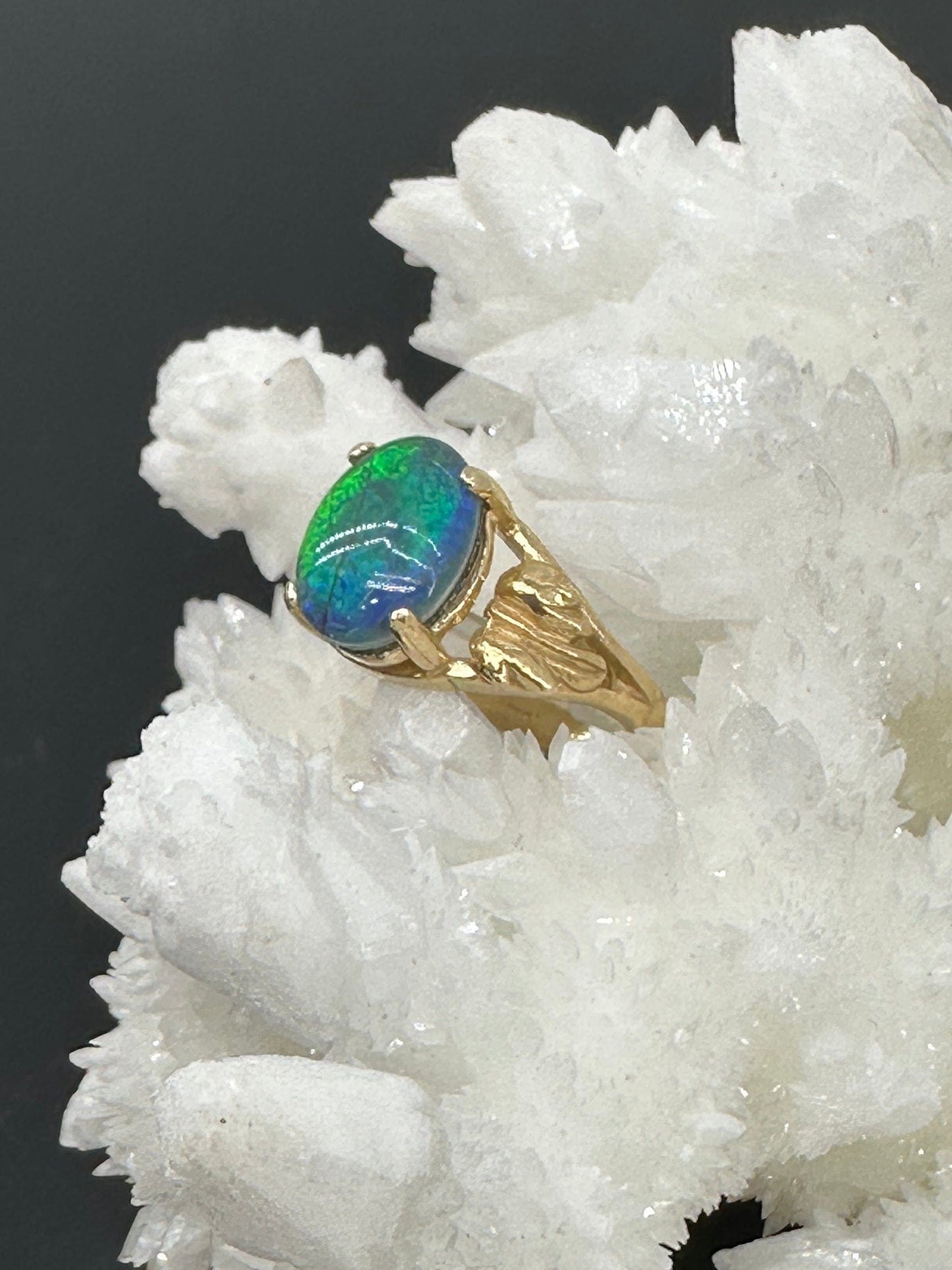 Gold ring with a blue-green opal on a white crystal background