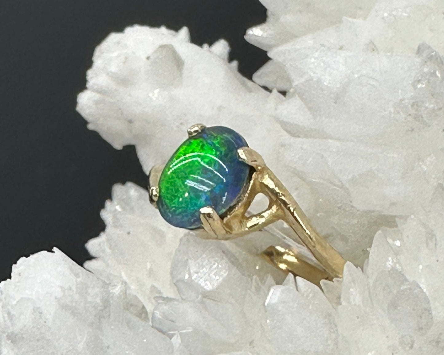 Gold ring with a green and blue opal stone on a white crystal background
