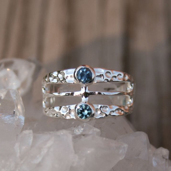 Silver ring with 2 Montana sapphires in a wide band with negative space and hammered texture. 