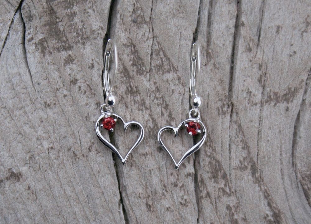 Heart earrings with red gemstone on wood