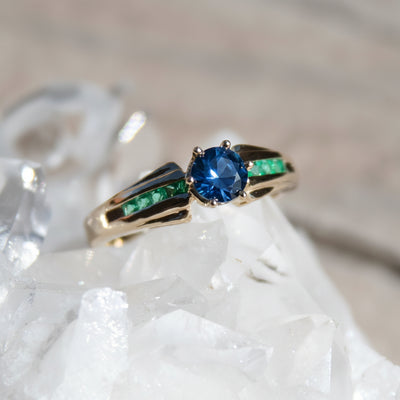Blue sapphire and emerald ring, fold with flared edges around the main large sapphre. 