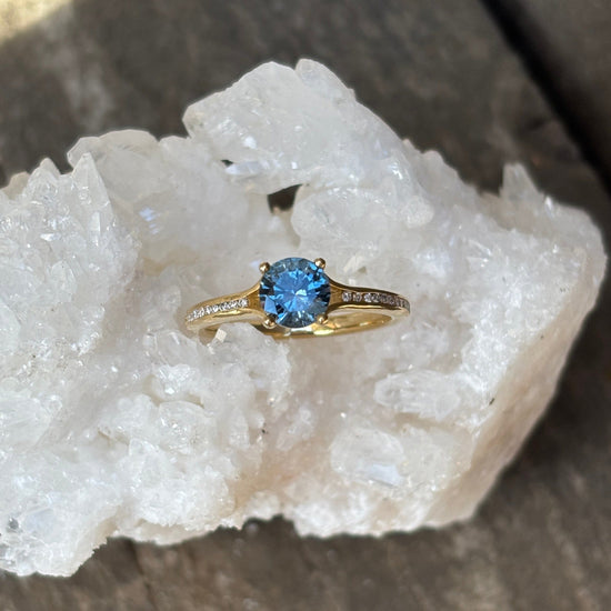 Gold ring with channel set diamonds showcasing a large Round Montana sapphire. 
