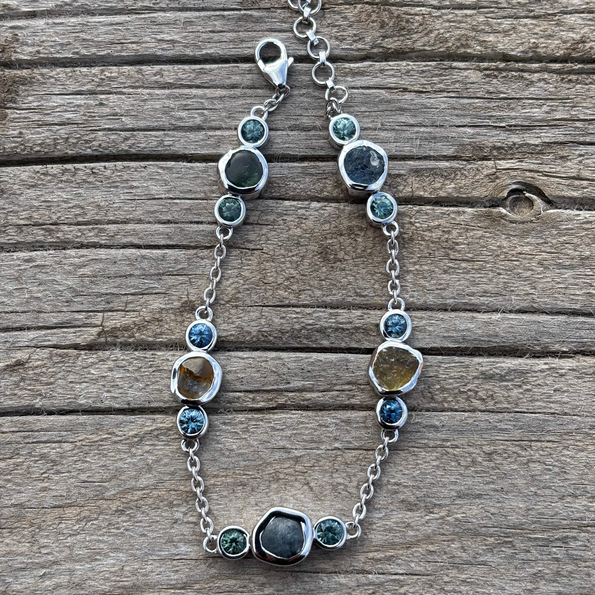 White gold chain style bracelet with cut and uncut sapphires on a wooden surface