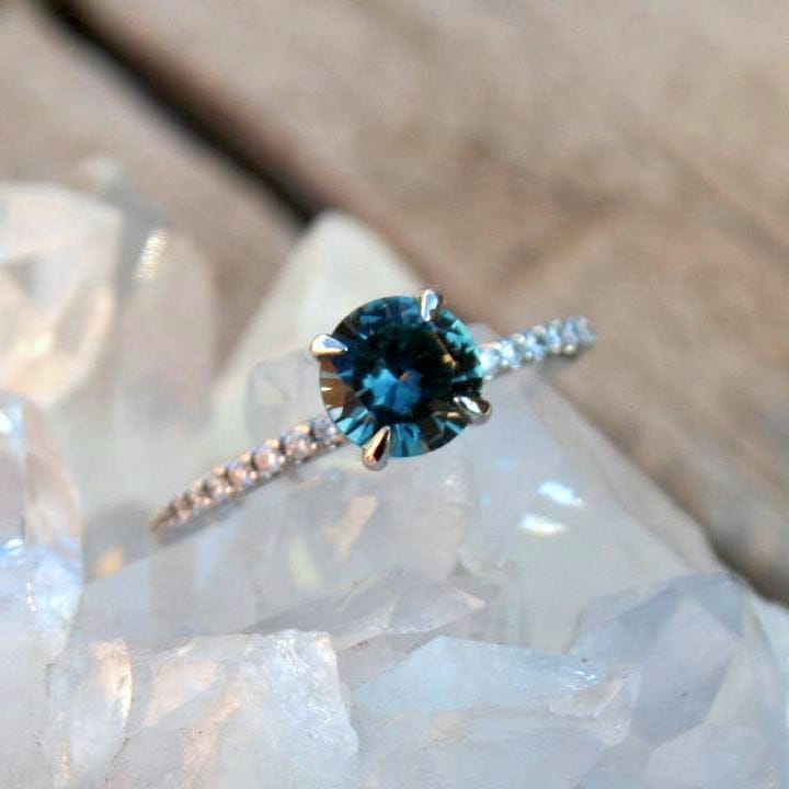 Teal Montana sapphire ring with diamond band on a crystal surface 