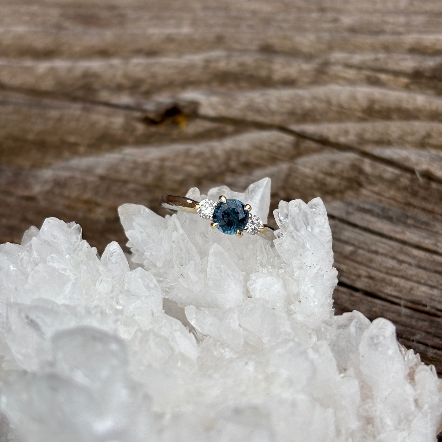 Ring with a large deep teal Montana sapphire with 2 diamond accents in two tone gold band