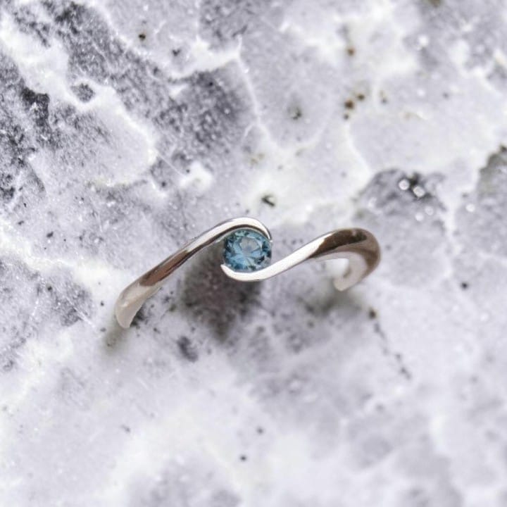 A silver ring bypass with a small round blue Montana sapphire set in a partial bezel.