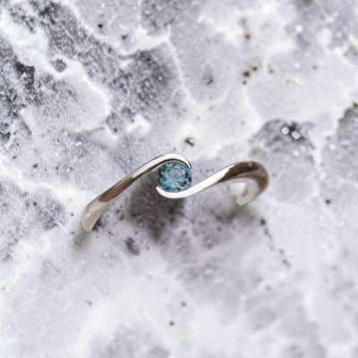 A silver ring bypass with a small round blue Montana sapphire set in a partial bezel.