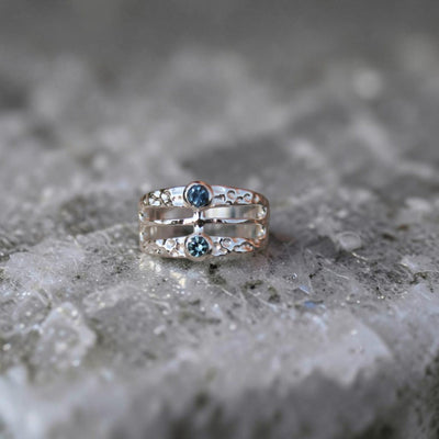 A wide band hammered finish ring featuring two Montans sapphires in different colors.  Geometric and modern looking. 