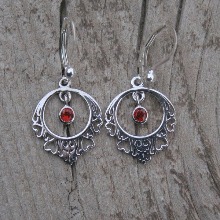 Silver earrings with open heart framed hoops around bezel set garnets