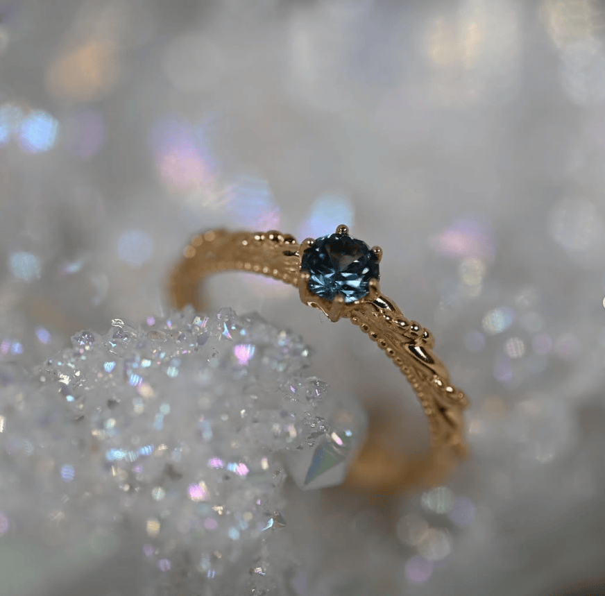 A gold ring with a round blue Montana sapphire, a pretty detailed band holding a solitaire stone. 