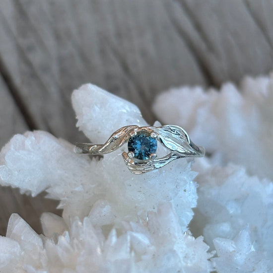 Silver ring with a blue sapphire in a leaf detailed band on a white crystal background