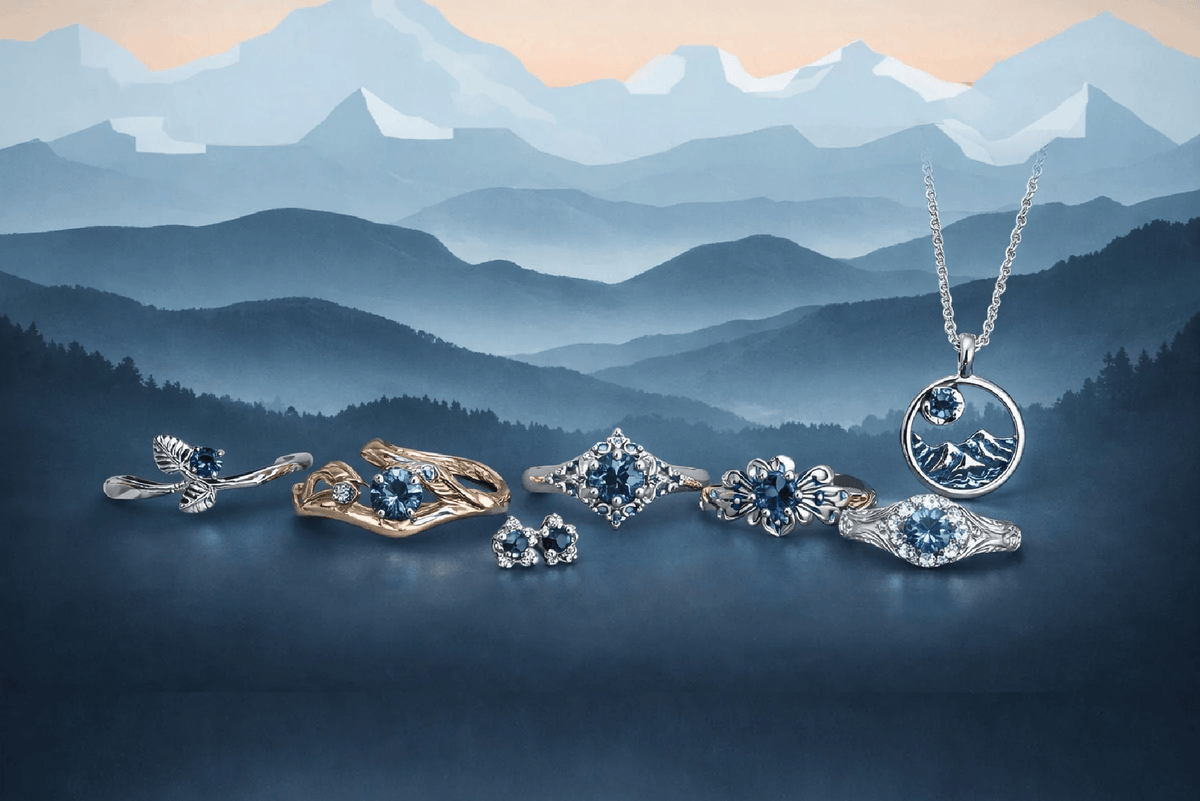 A jewelry set displayed against a stylized mountain landscape background, featuring a silver pendant necklace with a blue mountain motif, several silver rings with blue gemstones, and a gold ring with a blue gemstone.