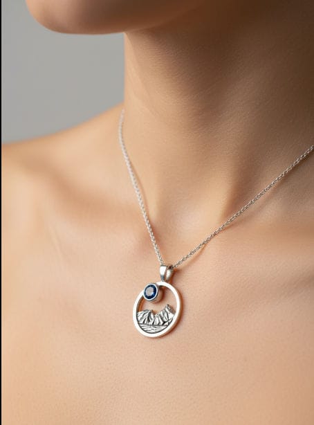 Silver necklace with a pendant featuring a blue gemstone and mountain design on a neutral background