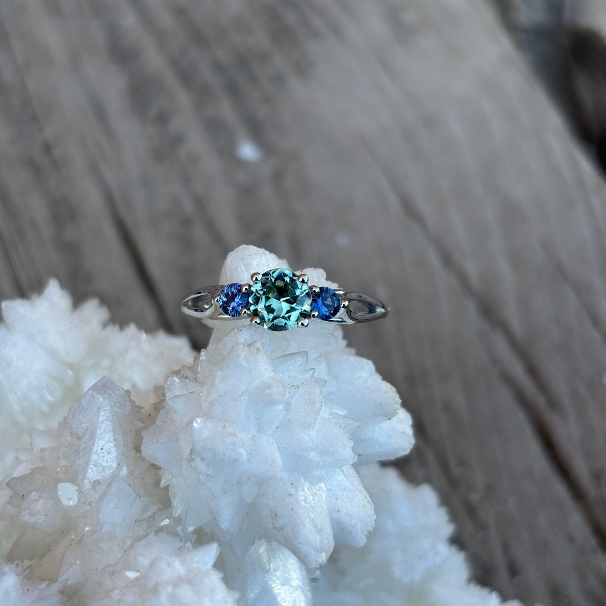 Green hued center with 2 yogo sapphires in a white gold engagement ring