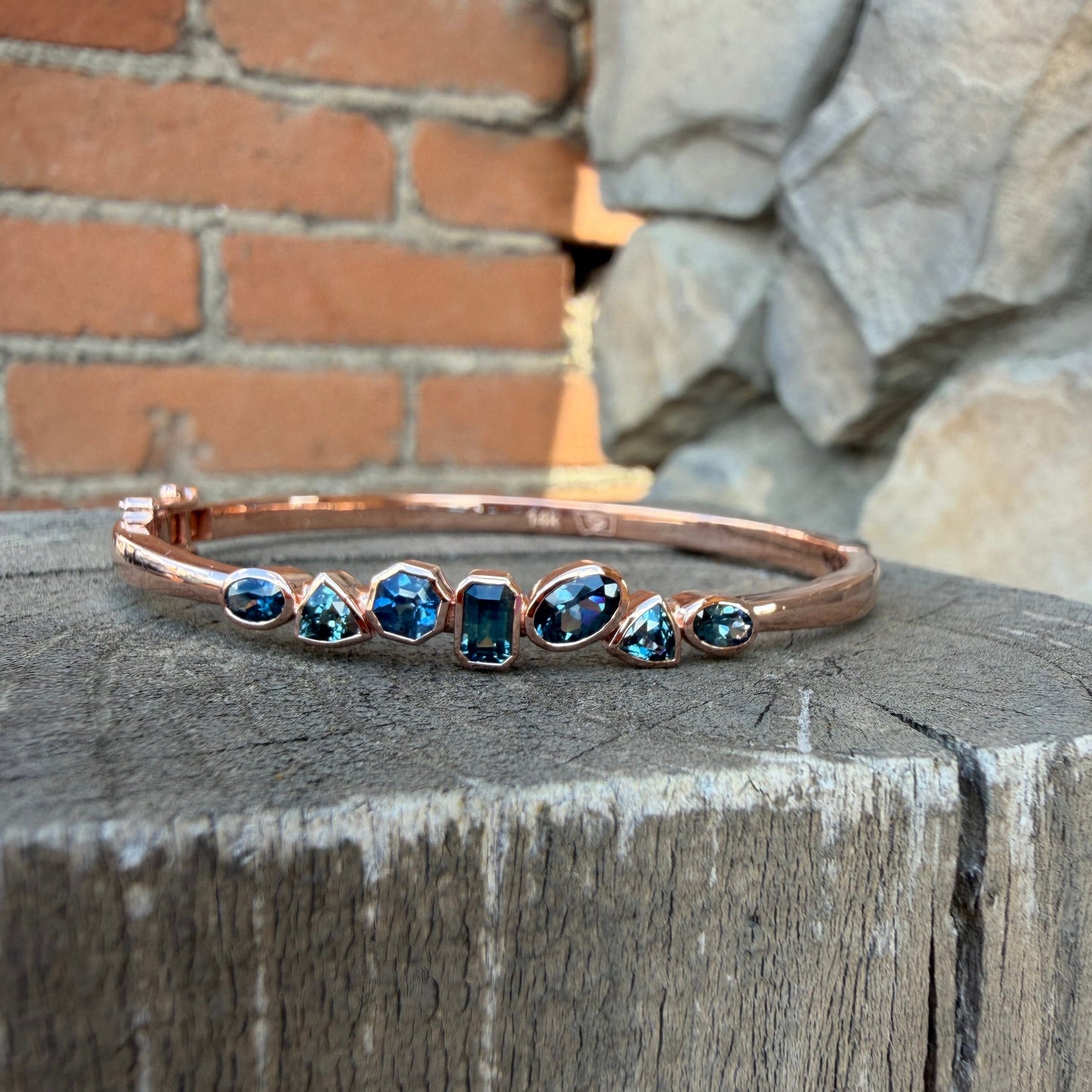 A rose gold bangle bracelet with seven blue Montana sapphires in a variety of shapes. 