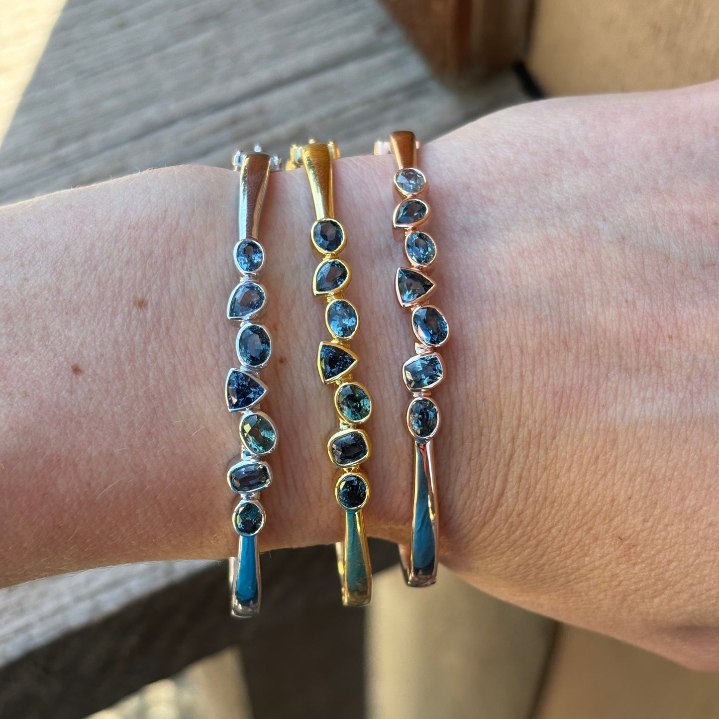 Gold bracelets with sapphires on a wrist against a neutral background