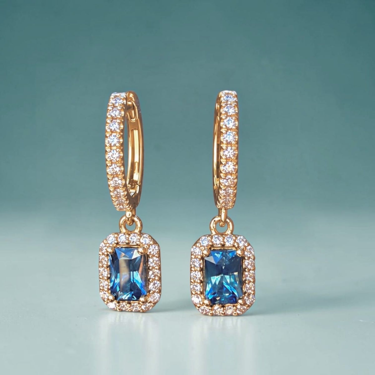 Ocean blue emerald cut Montana sapphires with natural diamond halos in 14k yellow gold dangle earrings.