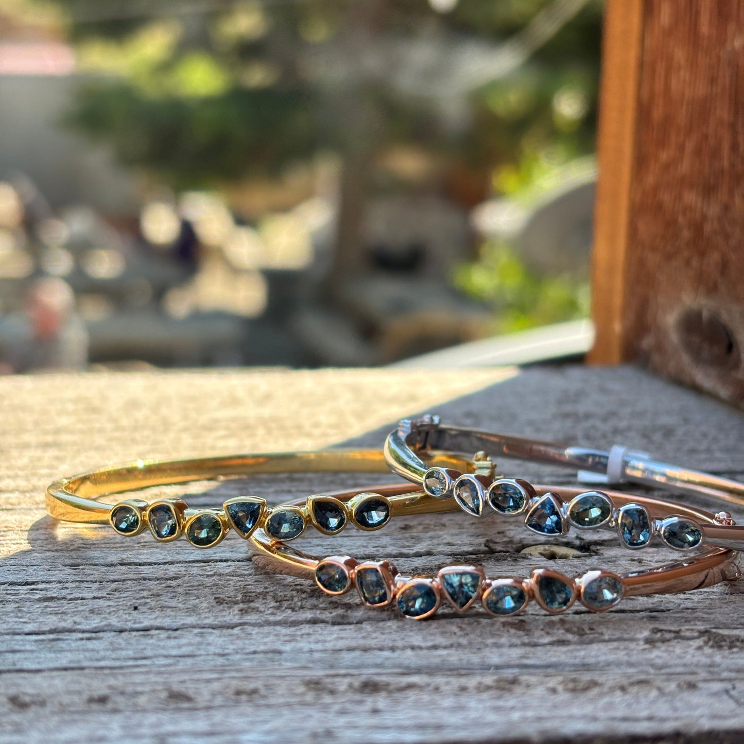3 sapphire bracelets in gold, rose gold and sterling with multi shapes on a wood background
