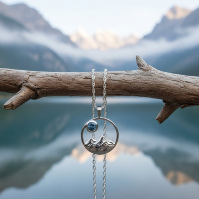 Silver pendant with mountain scene in a round frame.  Has a 4mm bezel set blue Montana sapphire. 