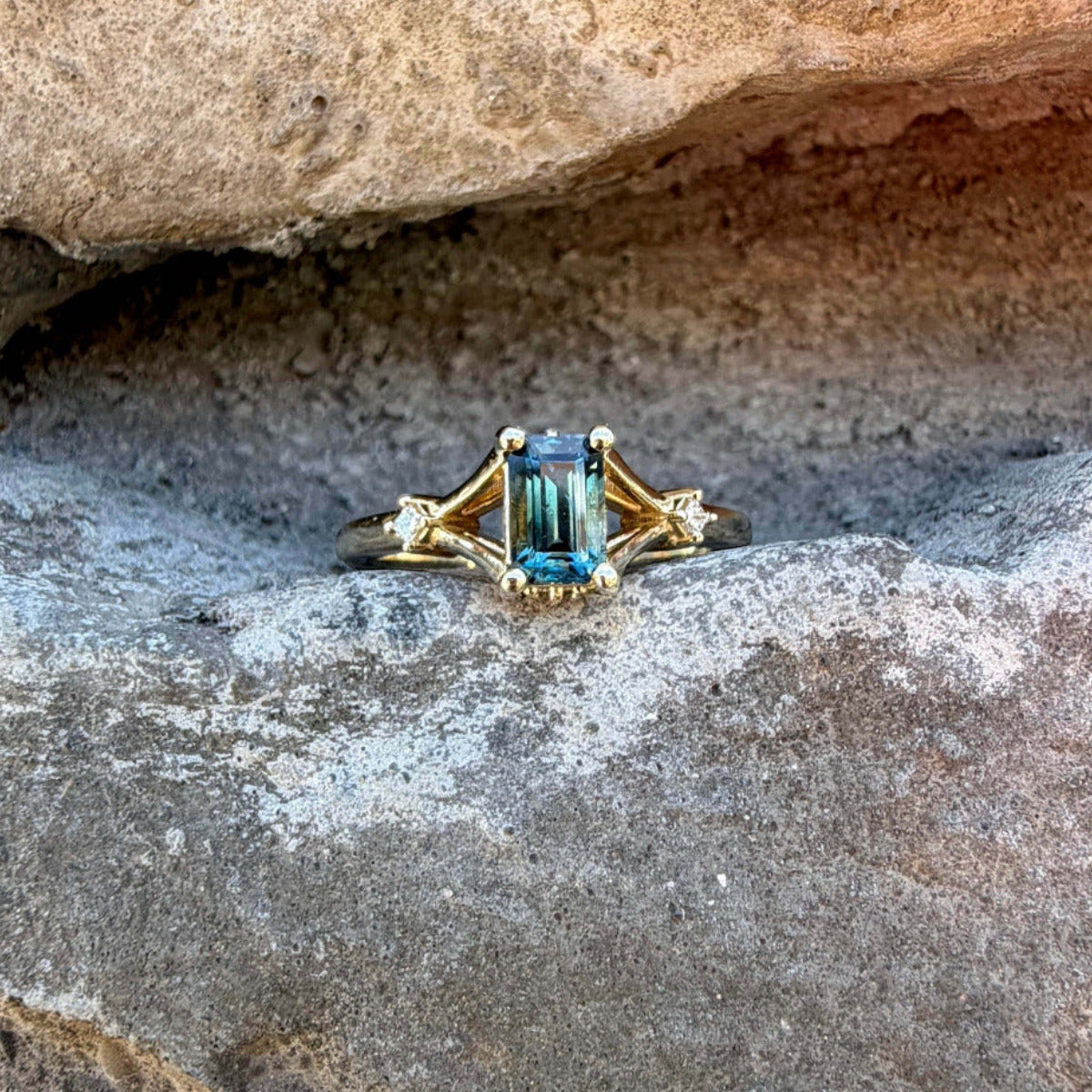 Emerald cut teal Montana sapphire ring in yellow gold with princess cut diamonds.