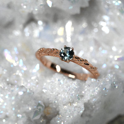 rose gold pretty detailed band with twists and beads holding a light teal Montana sapphre