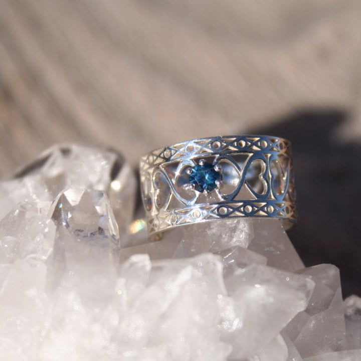 silver ring with heart filigree in a wide band and blue montana sapphire