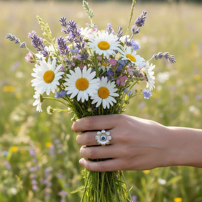 Montana Gems and Sapphire Jewelry sterling silver flower ring with a blue sapphire, held by a hand in a wildflower field