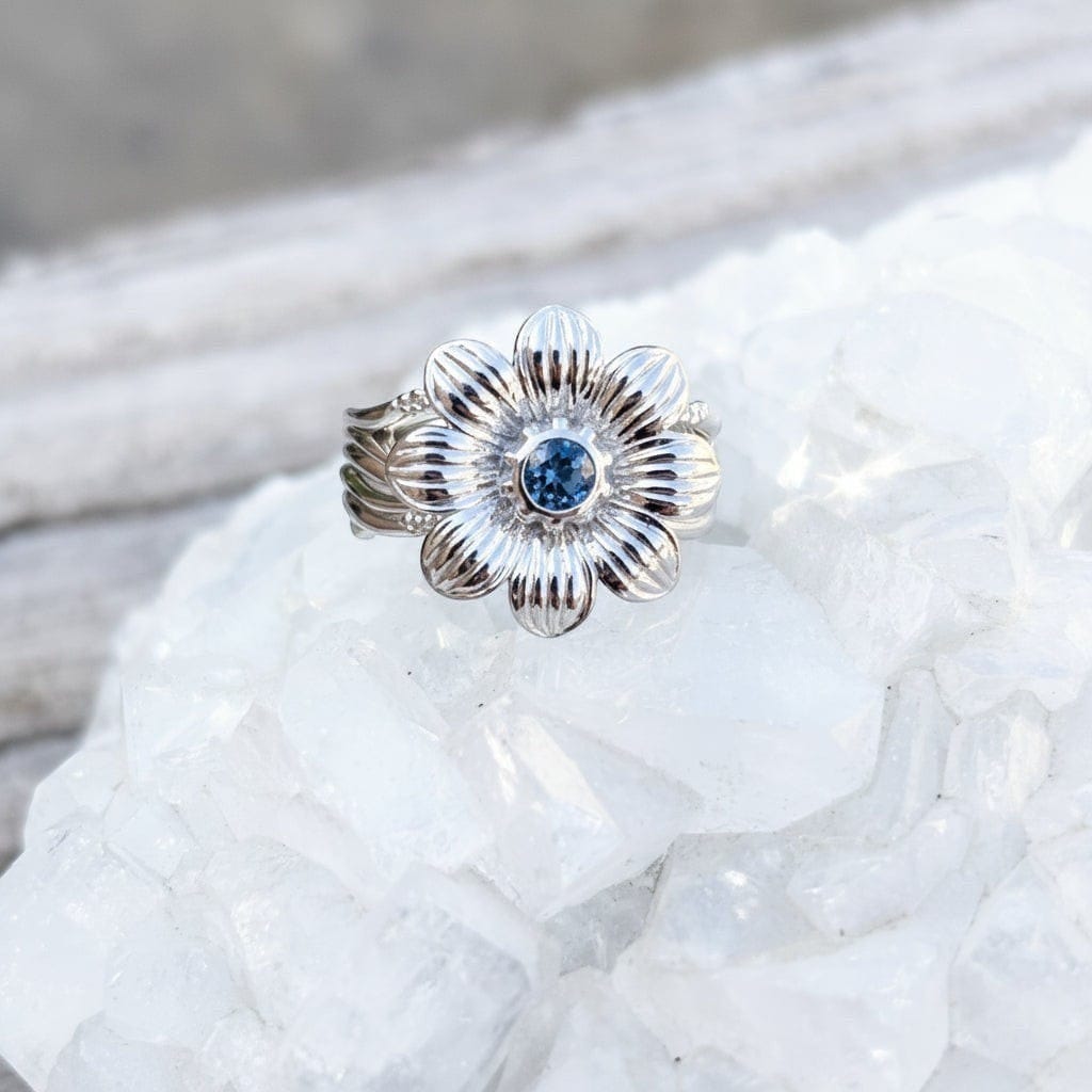 Silver flower-shaped ring with a blue Montana sapphire gemstone on a crystal background