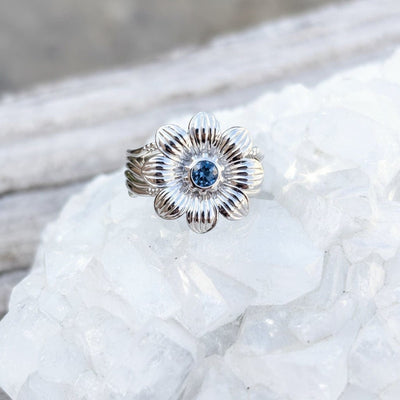 Silver flower-shaped ring with a blue Montana sapphire gemstone on a crystal background