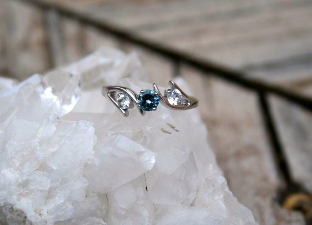Bypass style 3 stone ring with blue-hued Montana Sapphire flanked by 2 white Aqua Marines and set in sterling silver.